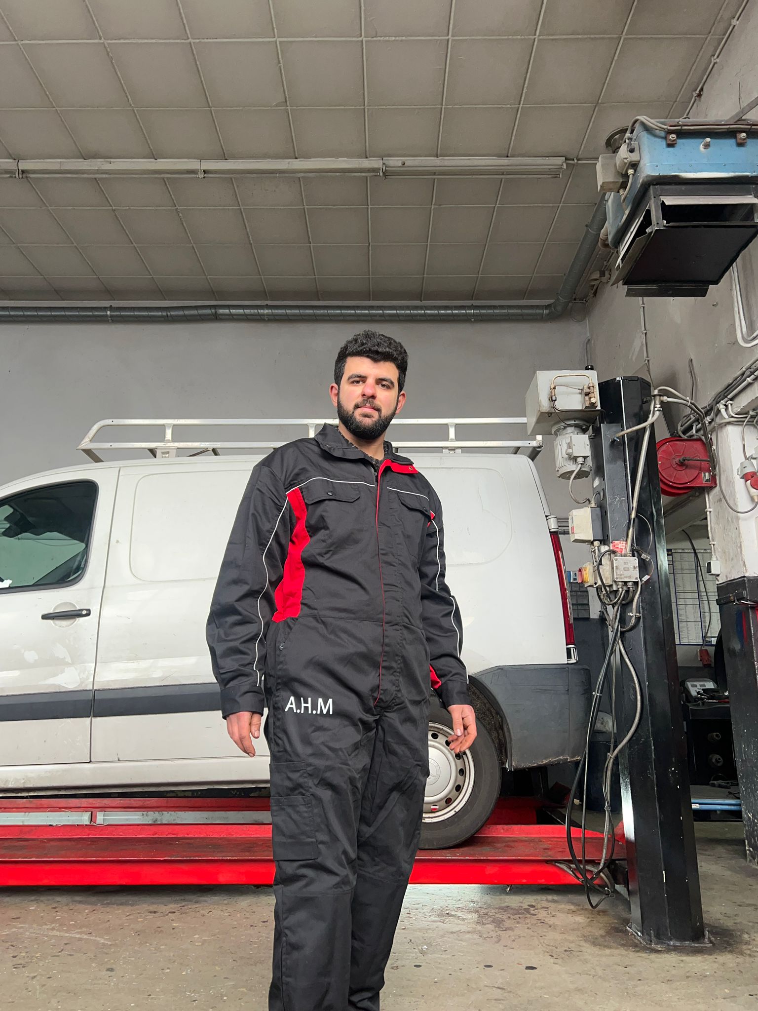 Monteur in de grijs-rode A.H.M-overall in de werkplaats, voor een bestelbus op de brug
