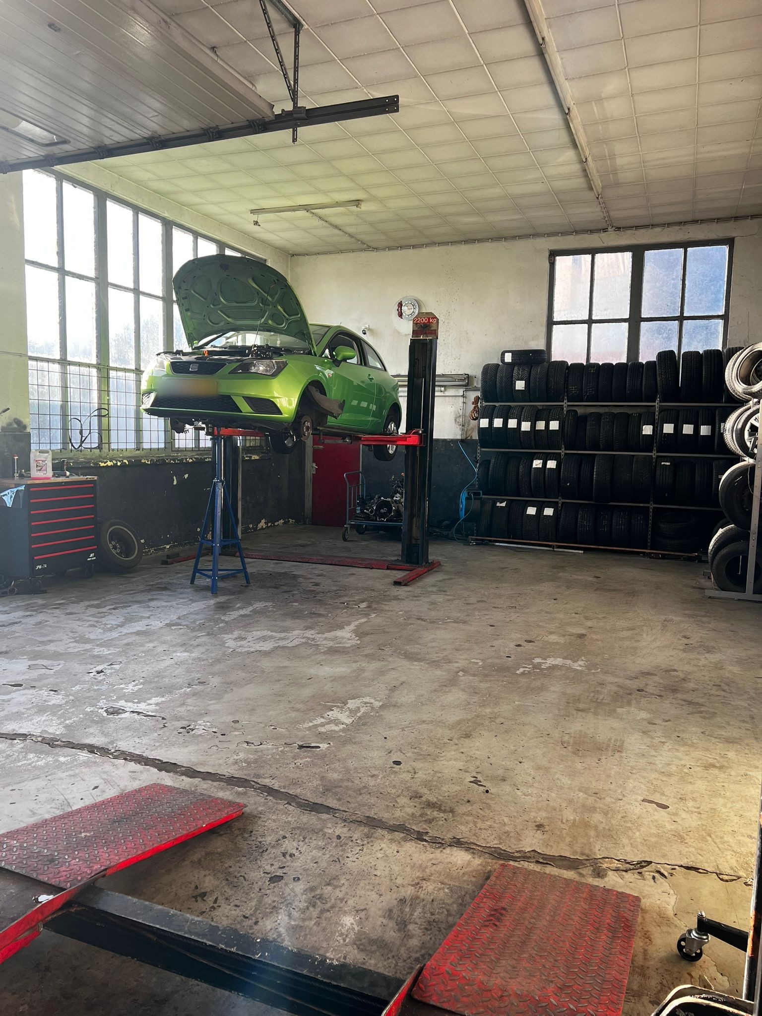 De werkplaats met een groene auto op de brug, bandenrek en grote ramen